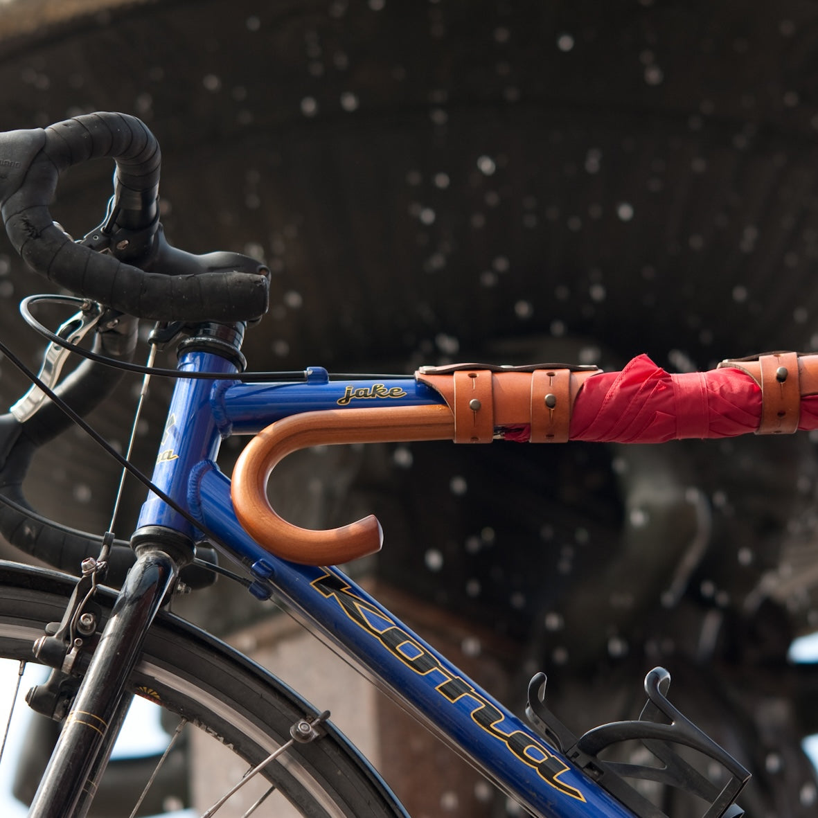 Bicycle with a red umbrella attached to the handlebar with leather cargo straps against a public fountain