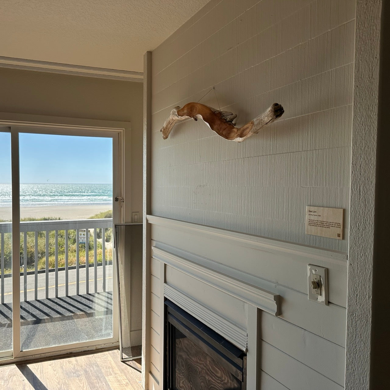 Room with fireplace, driftwood wall art, and view of beach and ocean.