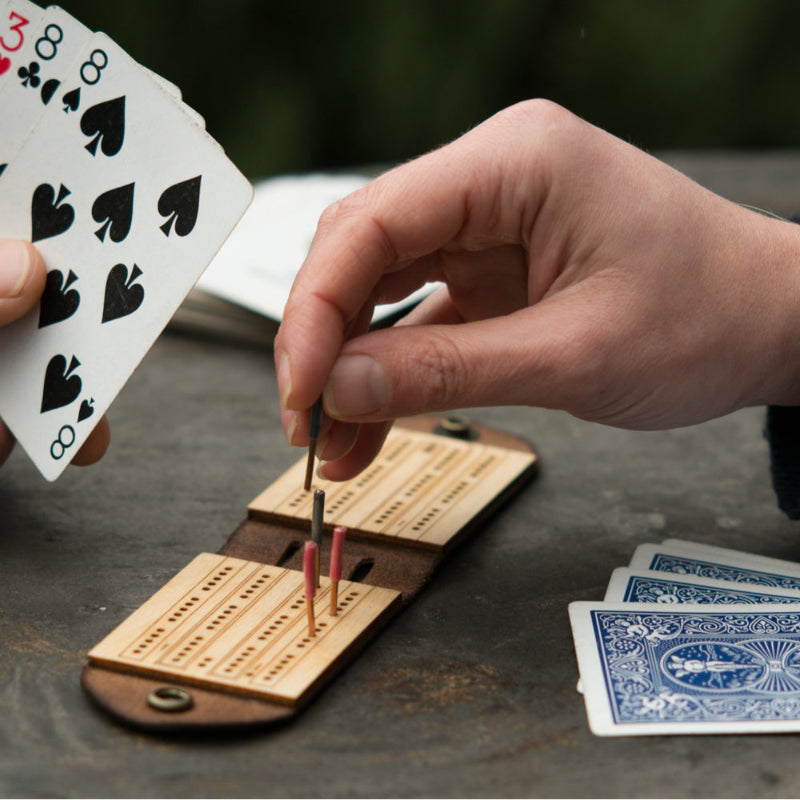 Two people playing on a small, foldable, wood and leather travel cribbage board