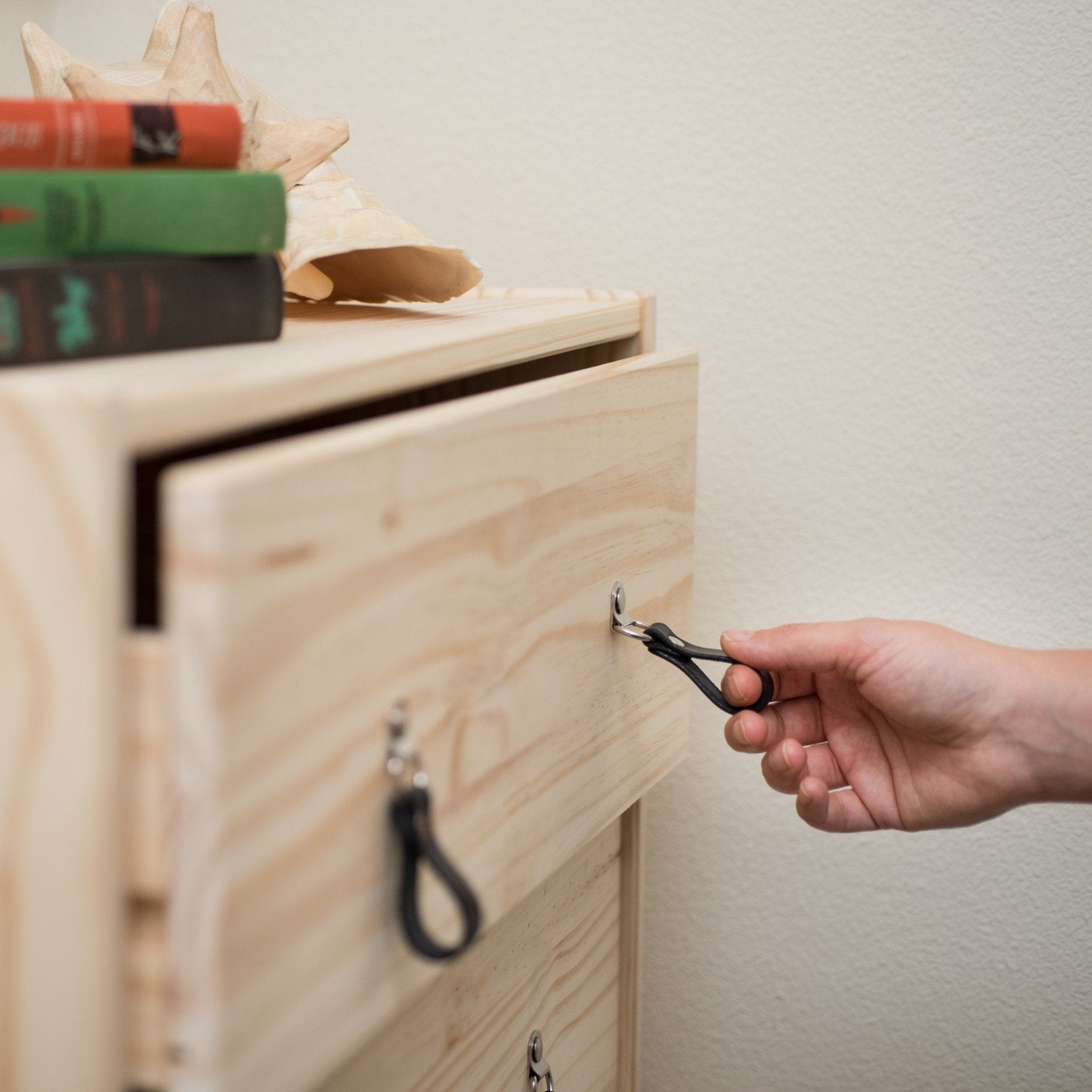 Woman's hand reaching out to an IKEA knotty pine wood dresser drawer and pulling it open using a small leather hinged handle in black leather with nickel hardware.