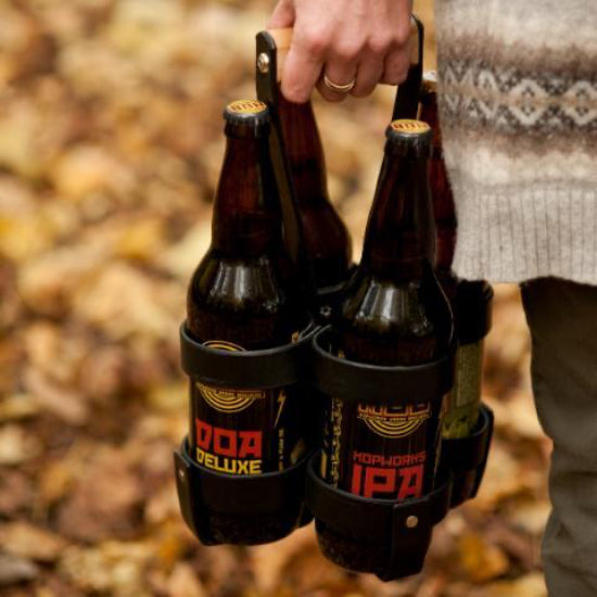 Woman's hand holding a carrier of four large "bomber" beer bottles or wine bottles in a leather strap box