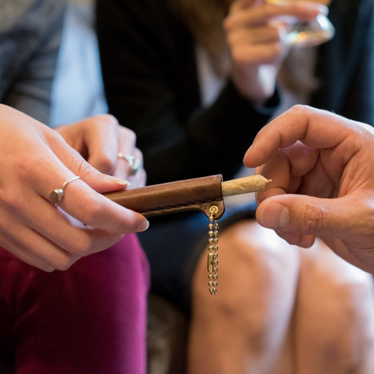Woman's hand passing a cigarette to a man with leather handroll case