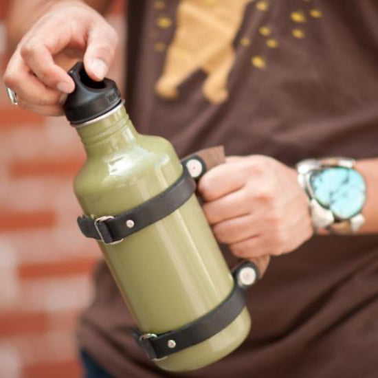 A man holding a large water bottle with a handcrafted leather and wood strap handle