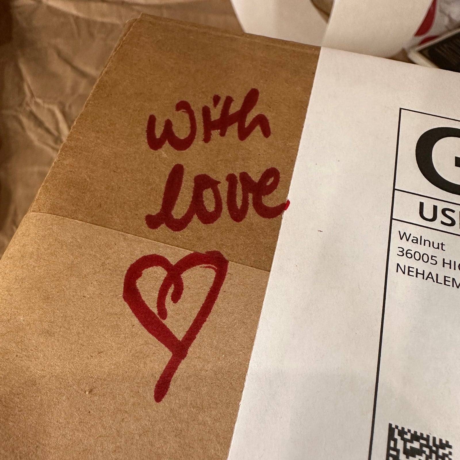 A shipping package with a handwritten note that says with love and a hand-drawn heart in red ink