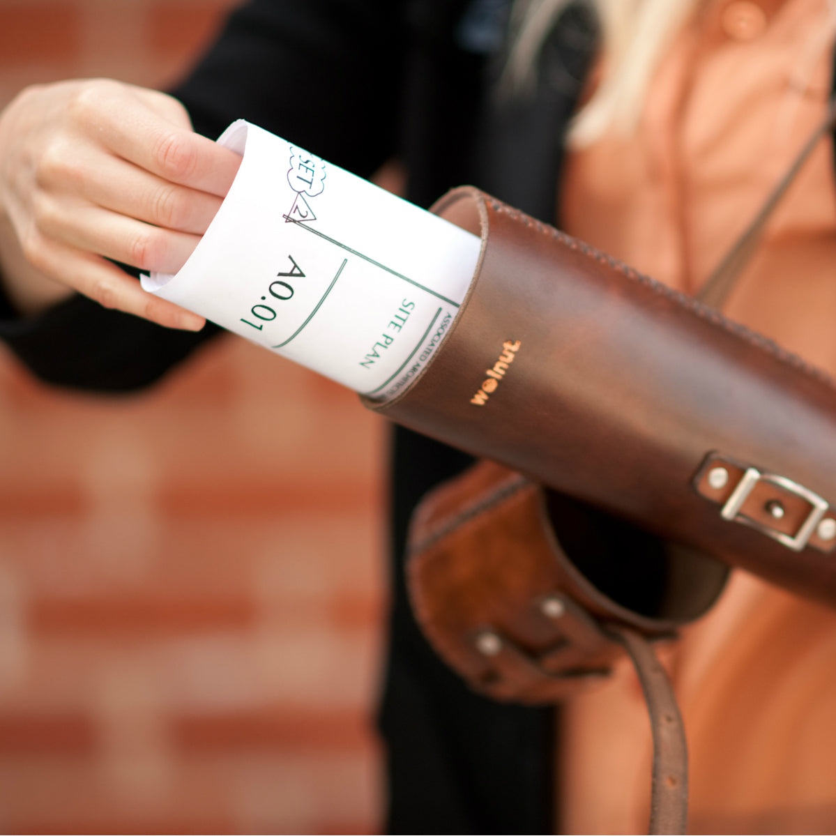Roll of large architectural documents being pulled out of a dark brown leather tube by a woman