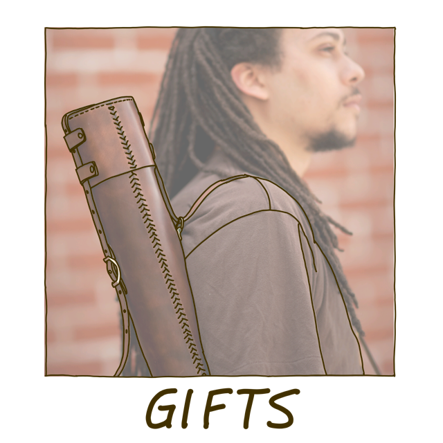 A man with beautiful long dreadlocks standing in front of a red brick wall wearing a brown t-shirt and holding a dark brown leather document tube over his shoulder for carrying large format prints and blueprints, with the word "Gifts" underneath