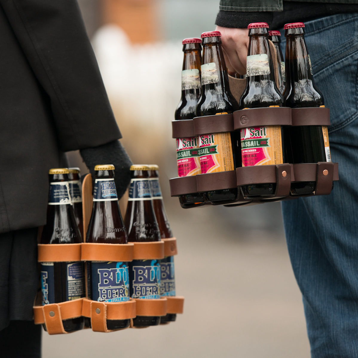 Two different people carrying two different six-packs of brown craft beer bottles with different labels in keepsake gift leather and wood 6-pack carriers