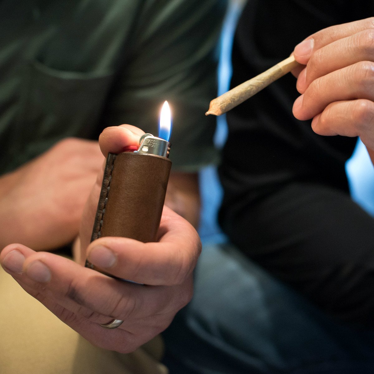 A man holding a light lighter in a leather lighter sleeve to a friend's handroll