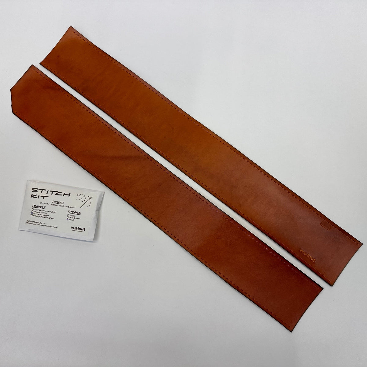 Two brown leather strips with a stitching kit on a white background