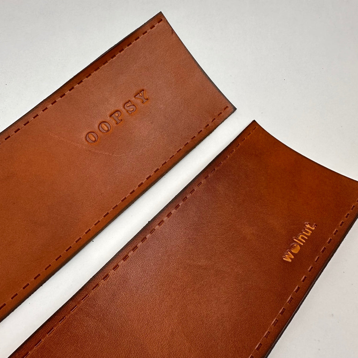 Ends of two honey brown leather sew-on wraps with stitch holes and the WALNUT logo and the monogram "OOPSY"