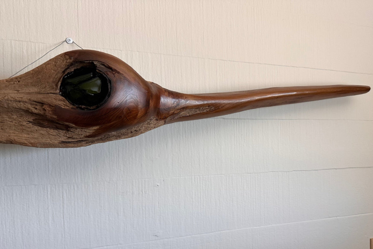 Driftwood sculpture resembling a bird on a wall with a plaque below