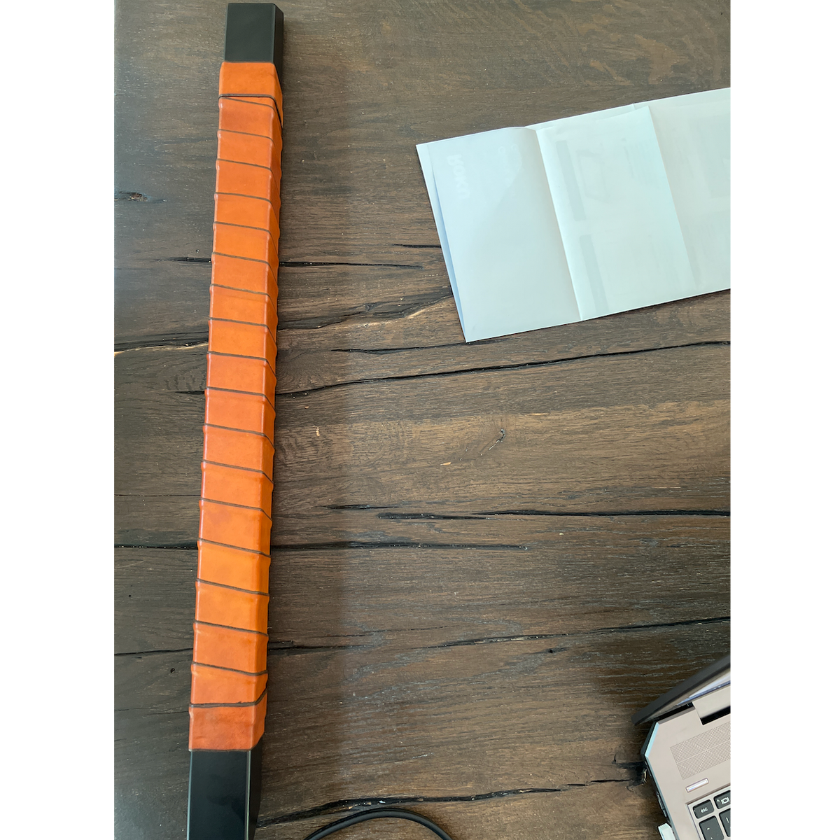 Customer photo of a square metal outdoor door handle wrapped in honey Oswego leather tape. The handle is just on a wood table surface before installation.