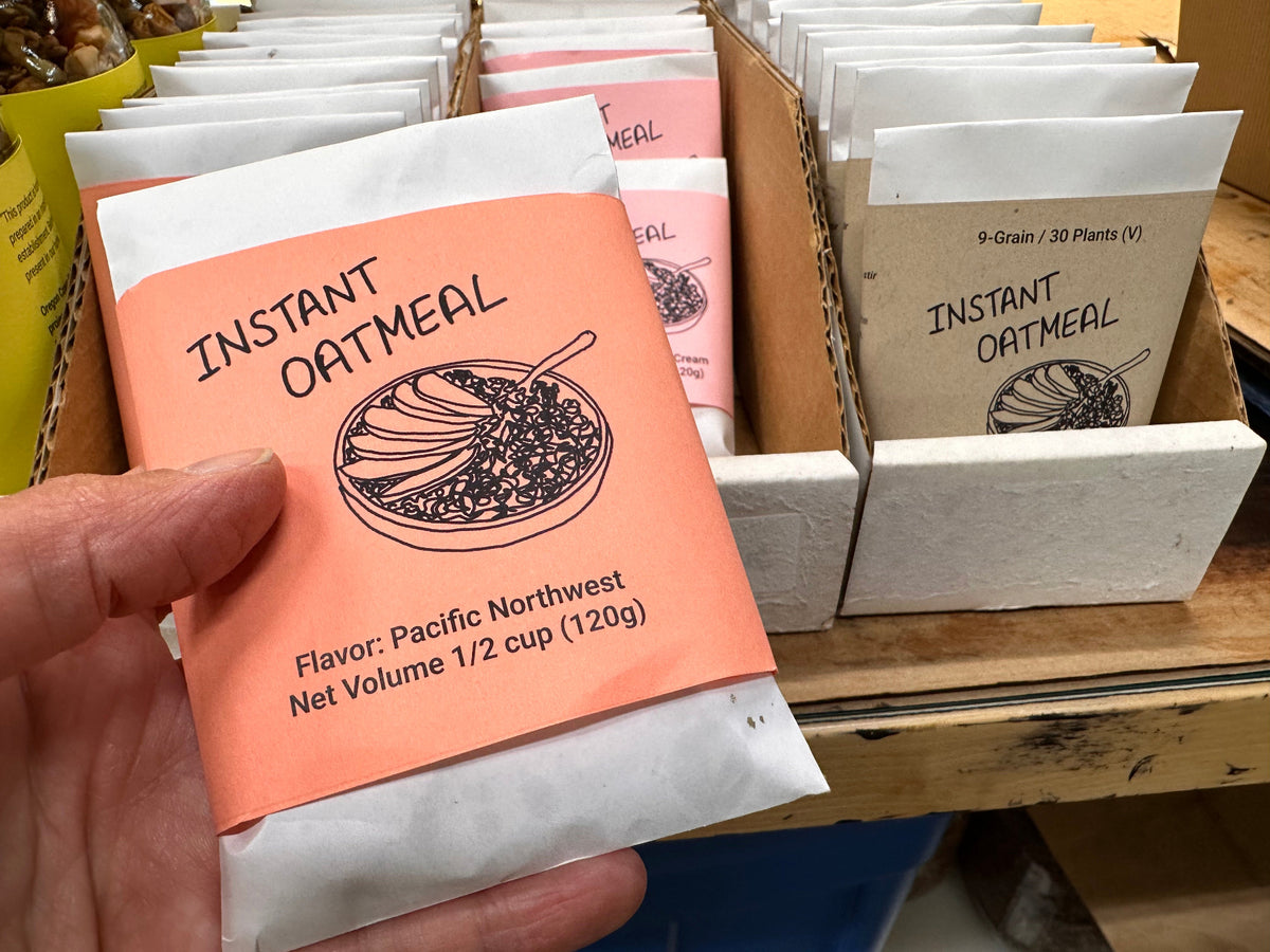 Instant oatmeal packets with a hand holding an orange packet labeled 'Pacific Northwest'.