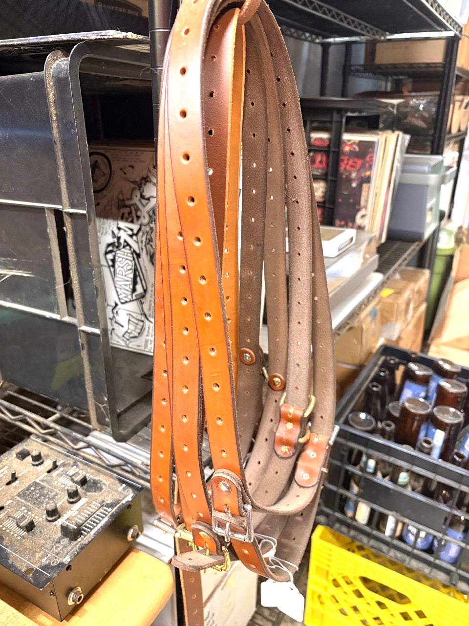 Leather belts hanging on a rack with a workshop setting in the background.