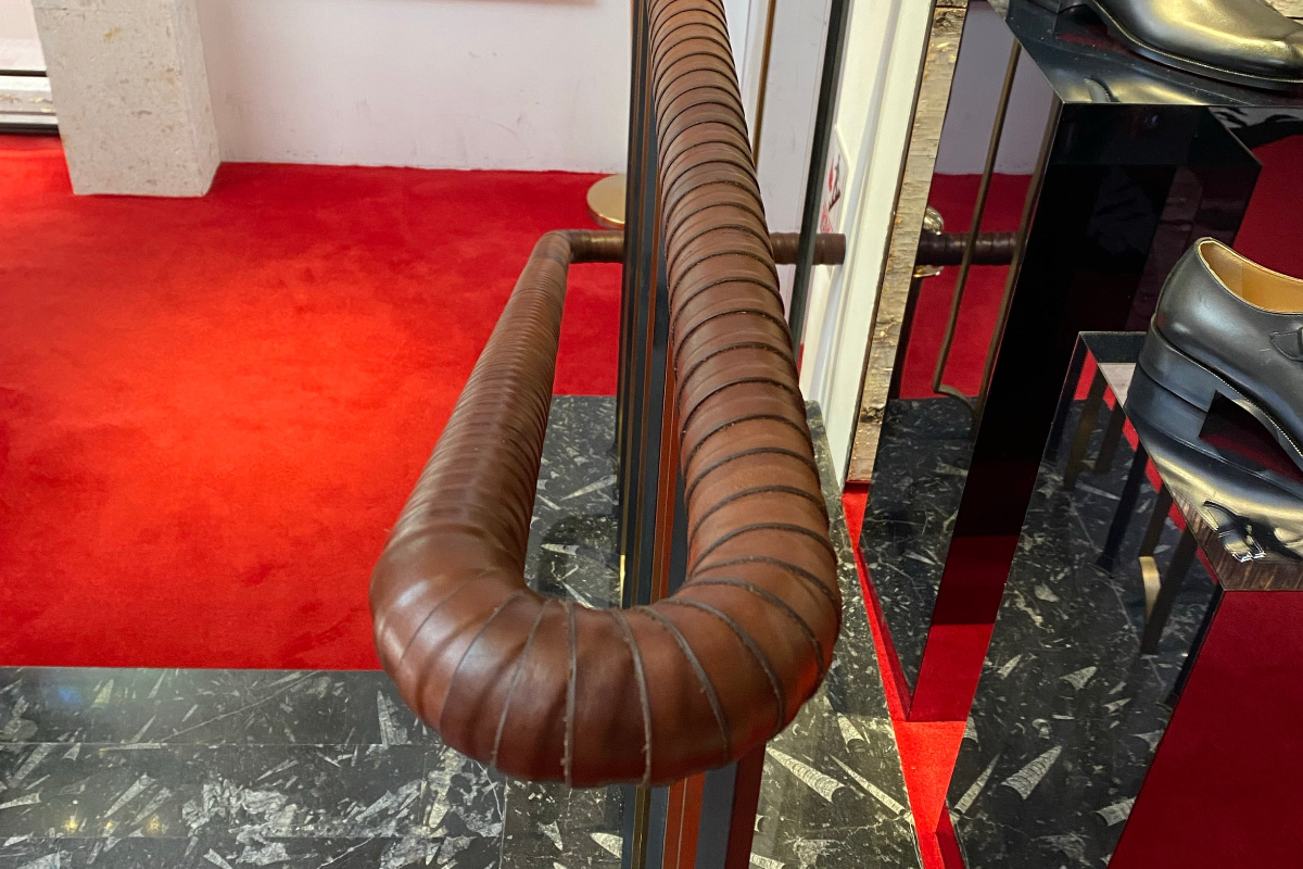 Brown leather wrapped handrail on a staircase with red carpet and marble floor, next to a high-end shoe display 