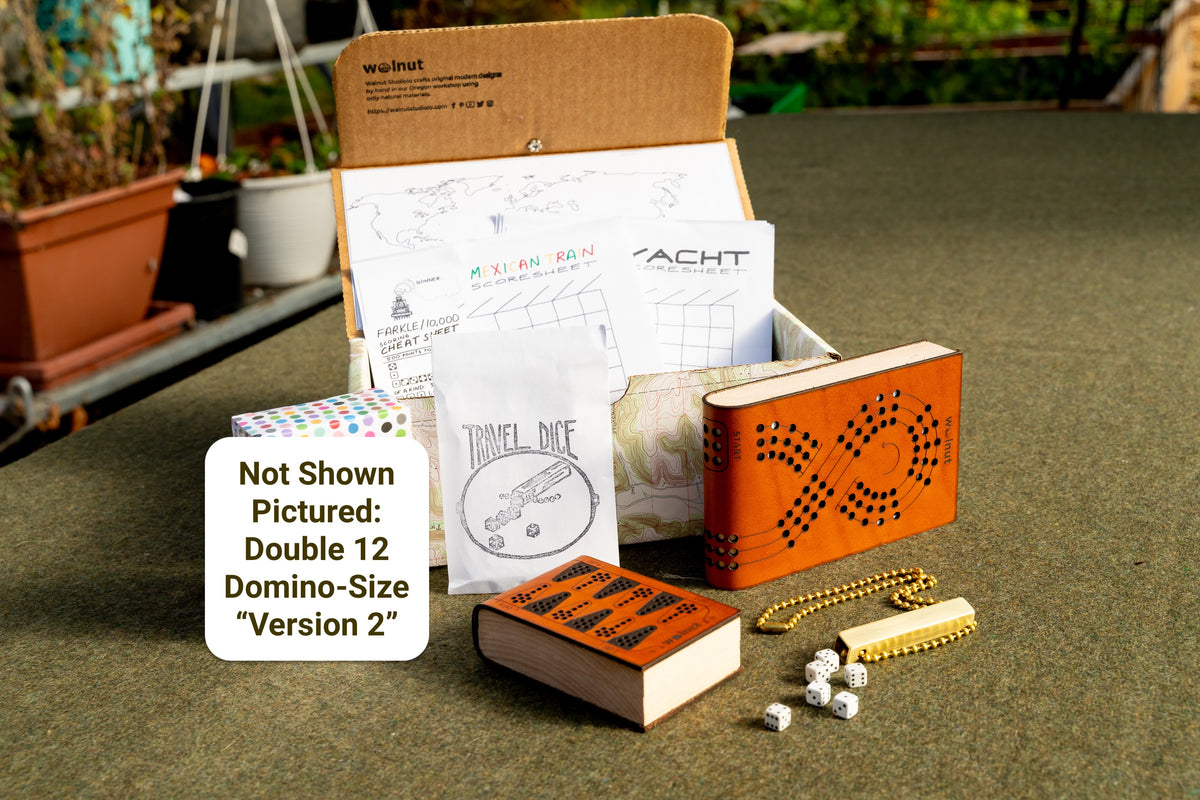 "Best of the Best" Travel games gift bundle shown with a handcrafted memory box, "places I've been" keepsake map, printed scorecards for Mexican Train, Yacht / Yatzy, and Farkle / 10,000 dice game, travel dice with brass tube, leather cribbage board, leather backgammon board, and "shown not pictured: double 12 travel dominoes playing cards version 2"
