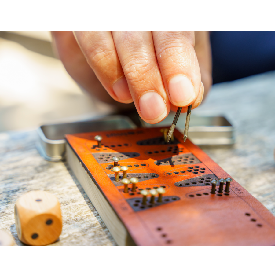 Close-up detail photo of a person's fingers grasping two brass game pieces from the travel backgammon board and moving two at once. 