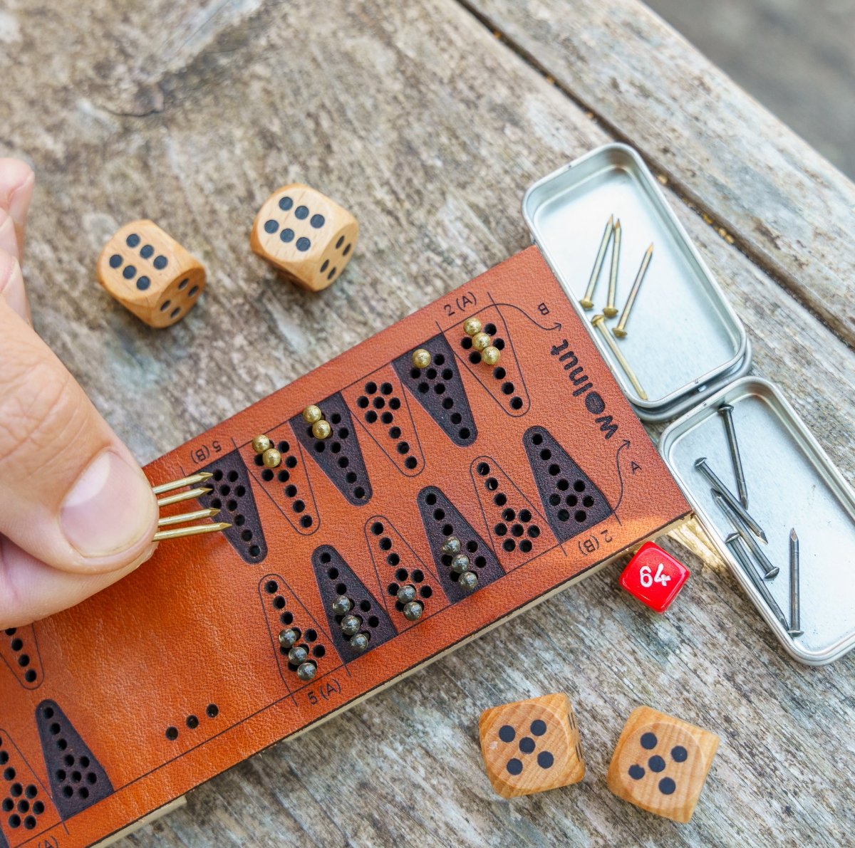 Close-up detail of a leather travel backgammon board laser quality and a man's hand moving four game pieces (nails) at once because he rolled a double 6 on the dice
