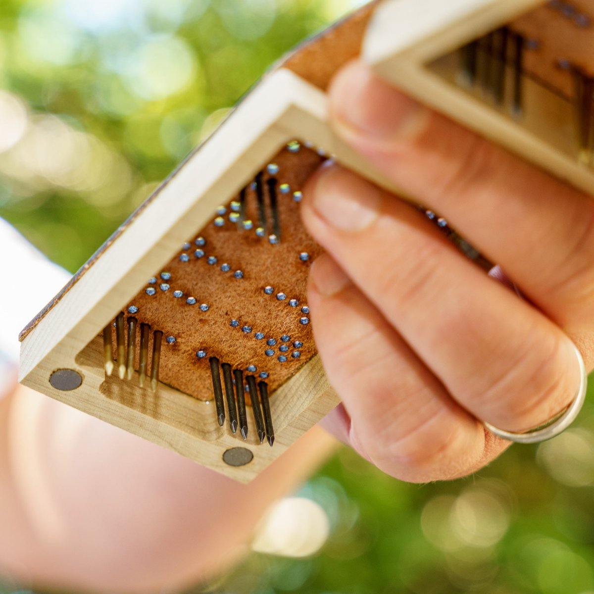 A person's hand holding up a travel backgammon board with the pegs or game pieces in play but the camera is looking up at the board from the floor so you can see the unfinished leather underneath and that the nail pieces go all the way through the leather, holding secure when moving