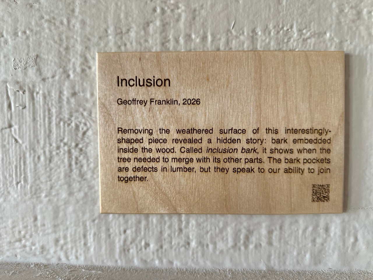Wood artist placard (plaque) on a textured white wall with artwork name, artist name, year, artist statement, and QR code 