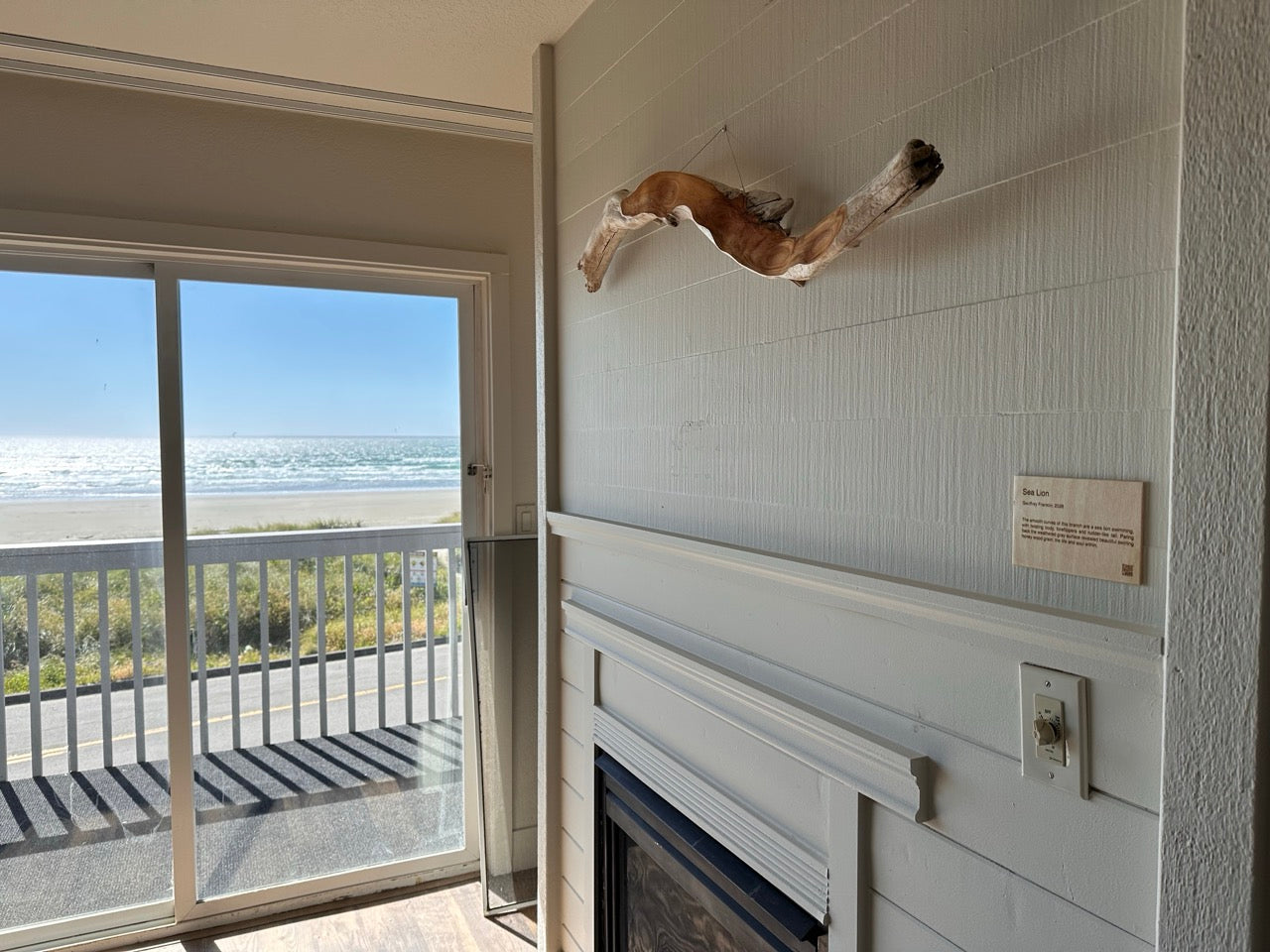 Room with a fireplace featuring a driftwood art piece hanging on the wall, sliding glass door to balcony, and view of ocean.
