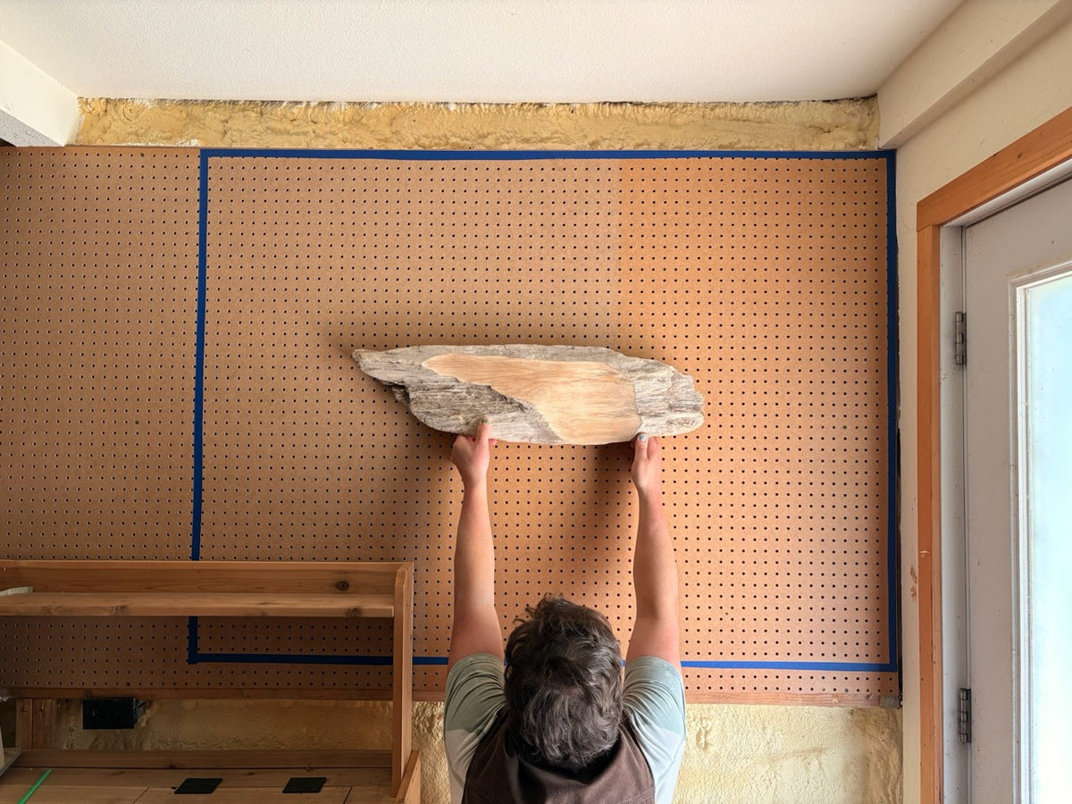 Geoff holding a driftwood art piece up to a mocked-up display wall using pegboard and blue tape