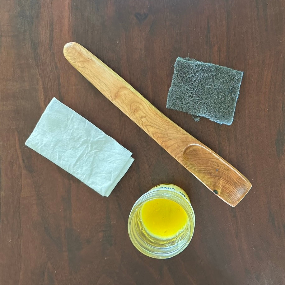 Still-life of a hand-carved wood spoon, abrasive hand pad, cotton buff rag, and flax wax in a rich gold color