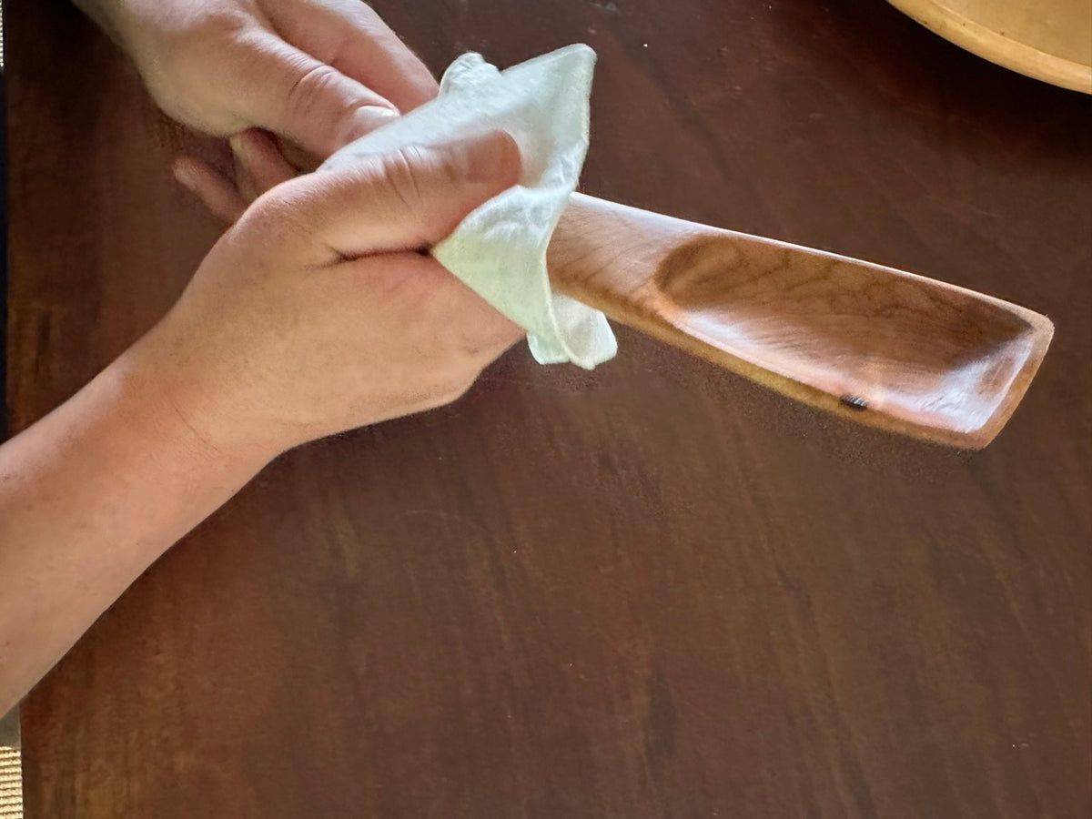 Hands in motion while rubbing a wood spoon with a cotton towel