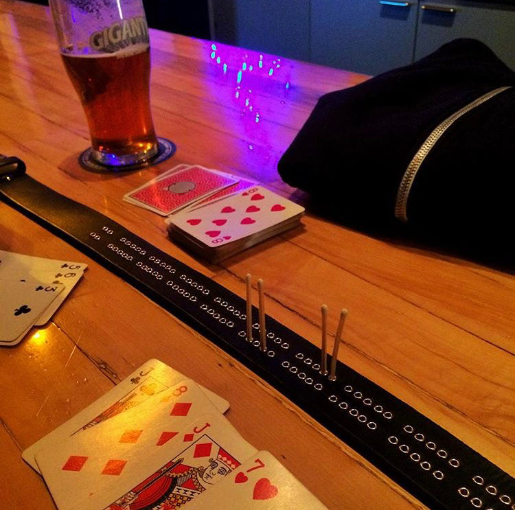 Customer photo of playing cribbage at the bar with the cribbage board belt, playing cards laid out, a glass of beer, and a black zippered pouch under neon lighting.