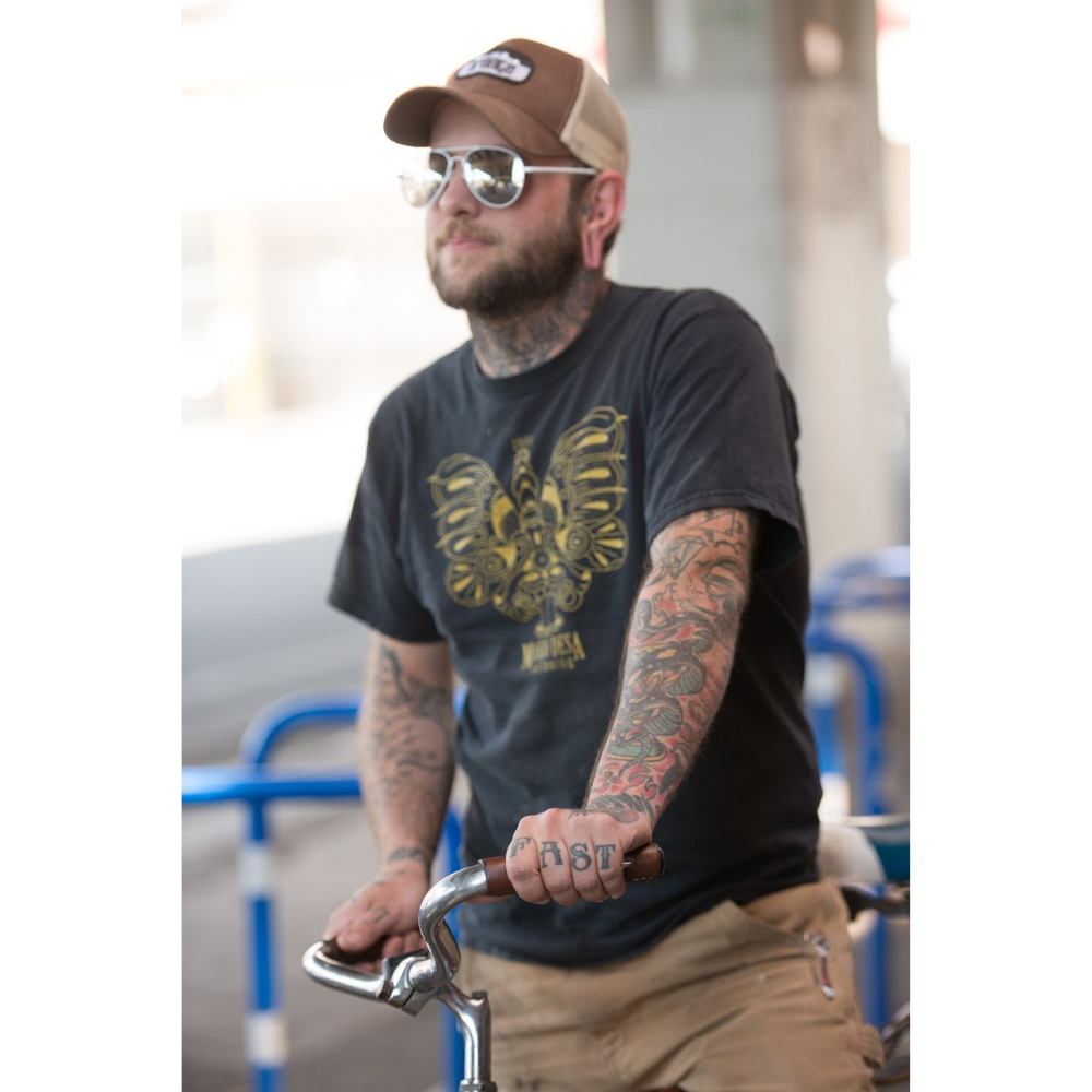 Tattooed man resting his hand on a bicycle city bar wrapped in a dark brown leather grip that has "porthole" round cutouts for finger holds. The man's hand tattoos say "HOLD FAST"