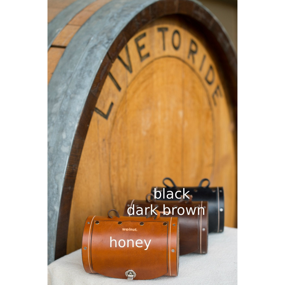 Front view of the three bag color variants: honey, dark brown, and black. The bags are displayed in front of a large barrel that reads "Live to Ride"