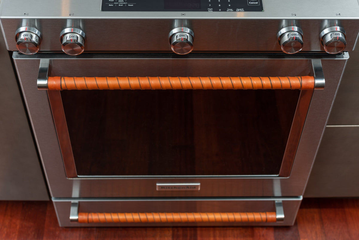 Looking down on an oven with both handles wrapped in honey vegetable-tanned leather. 