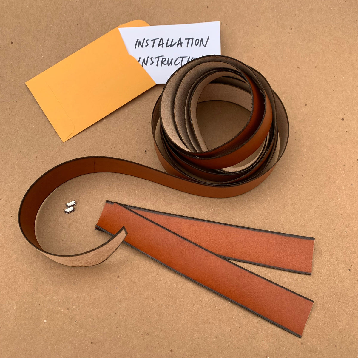 The kit as shown on a table surface, this is exactly what you'll receive: a long curled wrap, two extra bits for covering the ends, staples, and installation instructions. Walnut Studiolo Drawer Pulls Oswego Leather Wrap