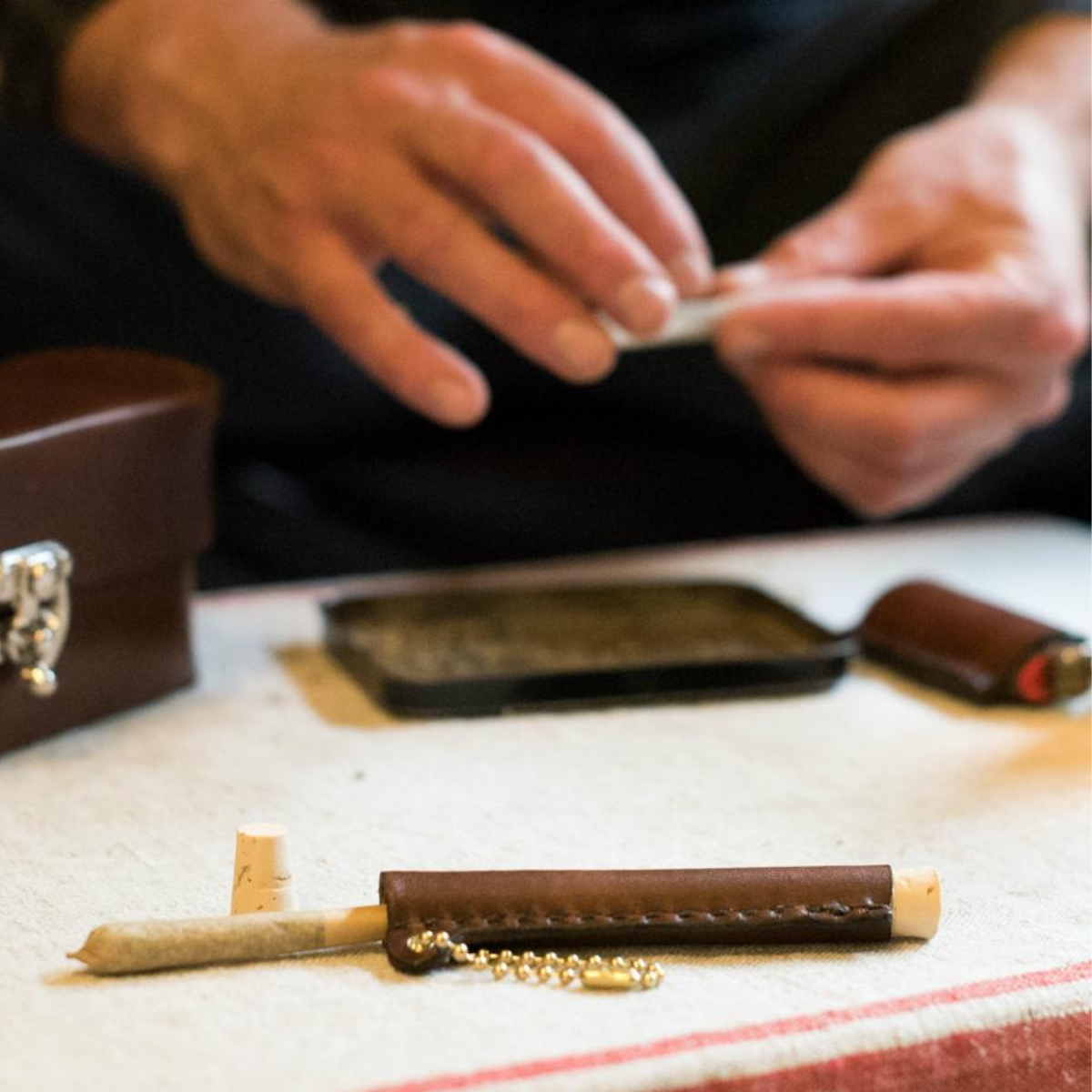 Man rolling a cigarette next to a leather "Classy Stash" box and leather lighter holder