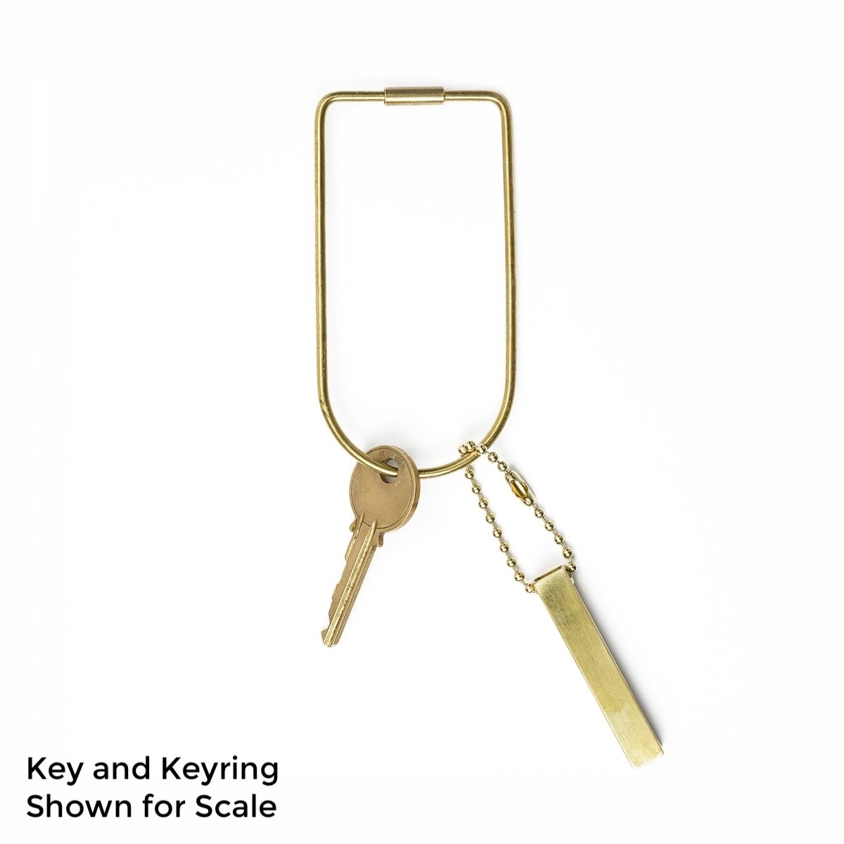 A brass keyring with a key and a set of brass travel dice attached to the keyring. The text on the photo says, "Key and Keyring Shown for Scale". 